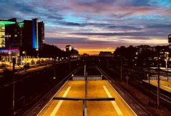 Sunrise at Amsterdam Sloterdijk train station, with the sky colored in pink and orange by the clouds and the railway tracks glowing in the morning light.